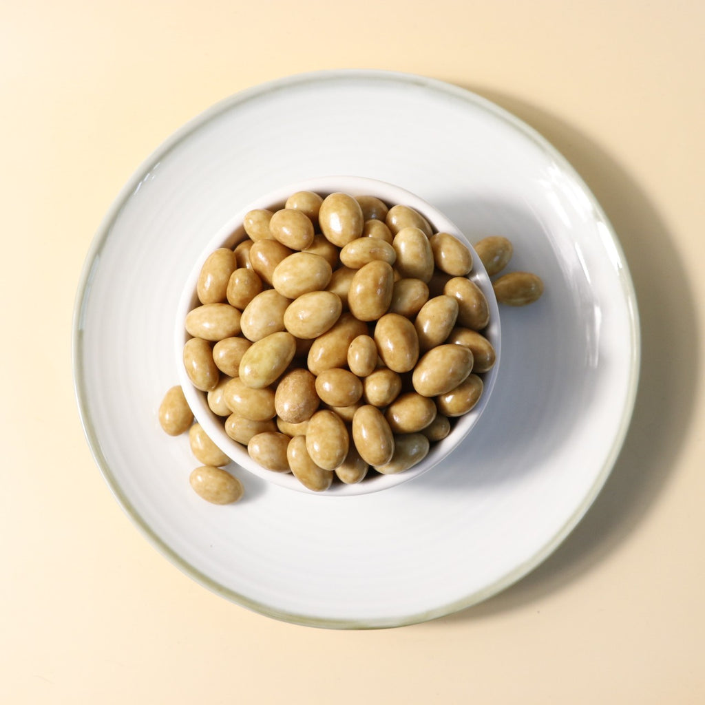Yathrib Caramel Pistachio Dragee showing glossy caramel coating with crushed pistachios on a white background.