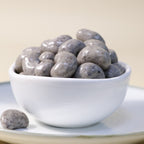 Creamy chocolate cashew dragee by Yathrib, close-up of glossy chocolate-covered cashew candies in a clear container.