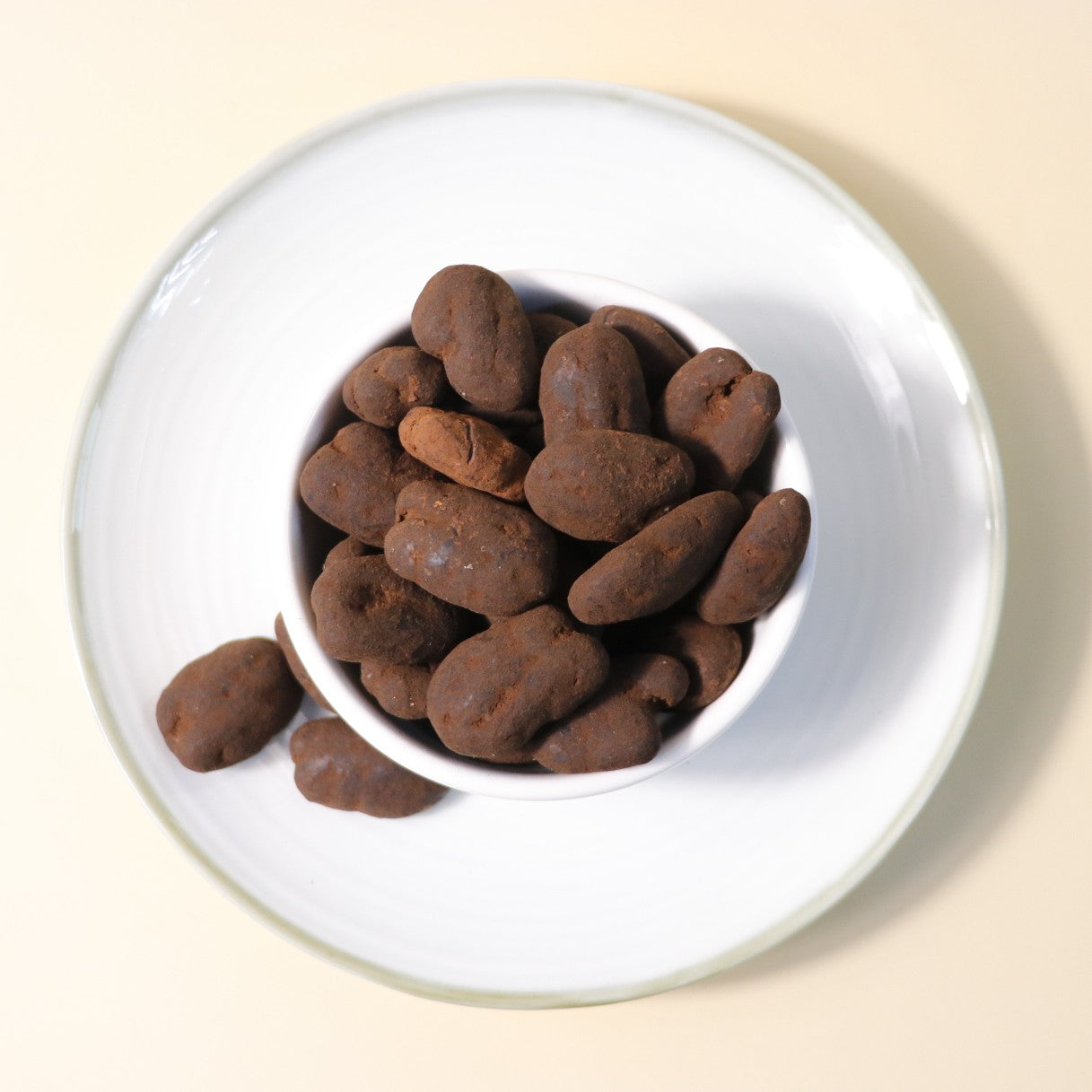Dark chocolate pecan dragee by Yathrib, featuring glossy chocolate-coated pecans on a white background.