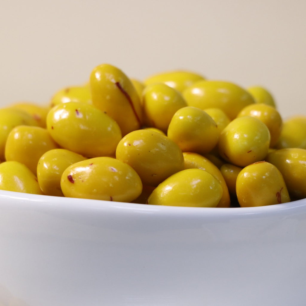 Yathrib saffron pistachio dragee showing glossy, golden-coated confections with visible pistachio pieces and saffron accents.