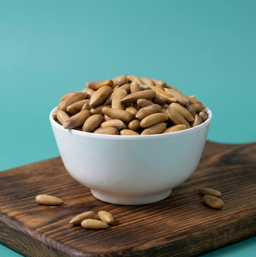 Yathrib shelled pine nuts in a clear bowl, showcasing small, creamy beige pine seeds with smooth surfaces, ready for cooking or snacking.